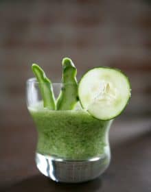 small clear glass of licuado de nopal smoothie garnished with a slice of cucumber and fresh nopal.