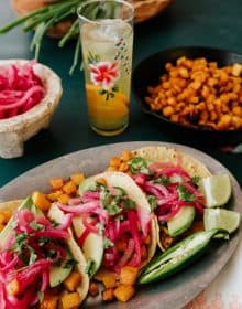tablescape with sheet pan roasted butternut squash tacos, a bowl of pickled red onions, and an orange spritz in a hand painted collins glass.