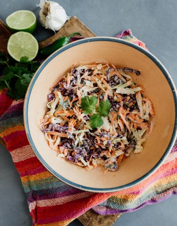 spicy coleslaw for fish tacos in a blue rimmed bowl on a rainbow striped kitchen towel.