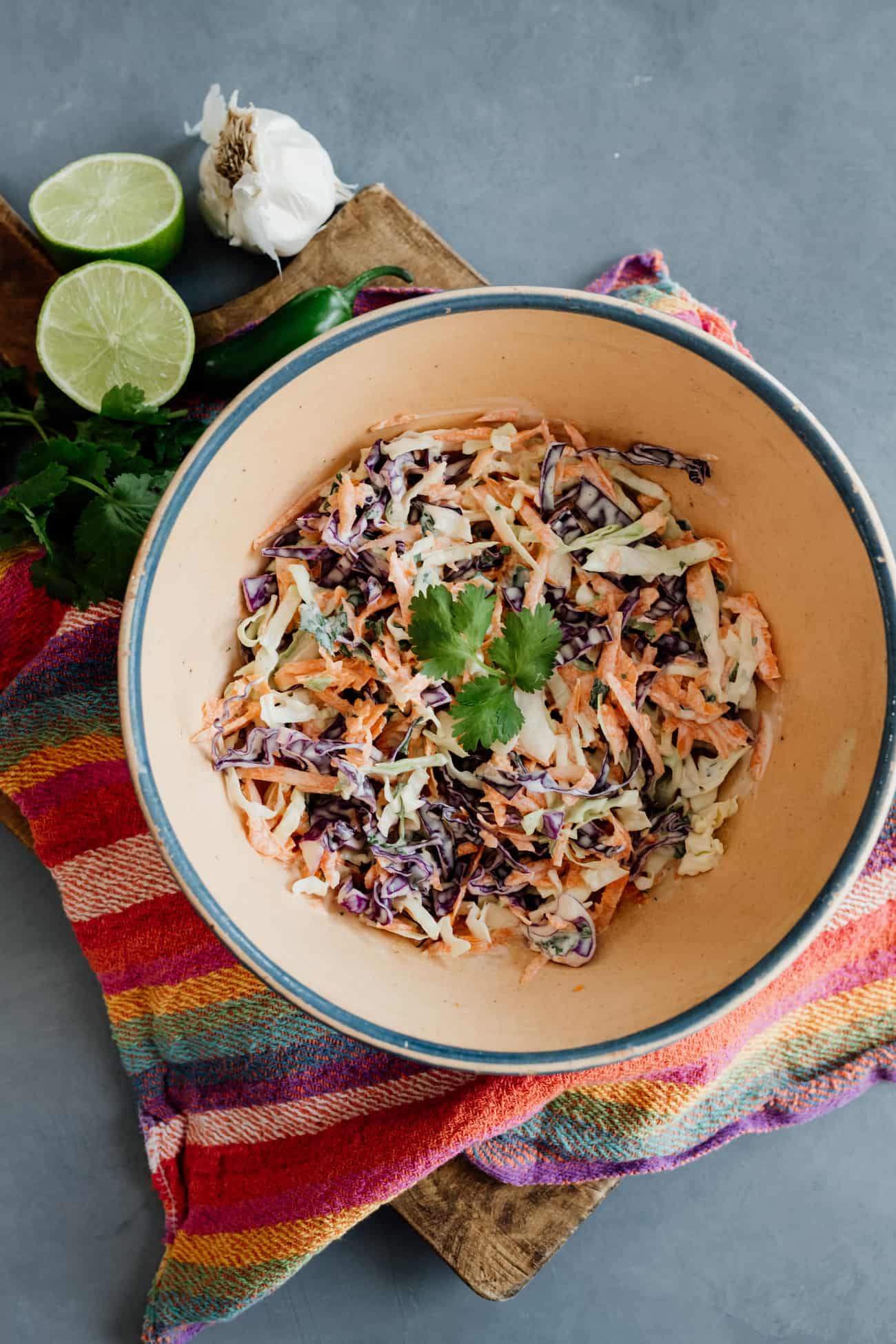 spicy coleslaw for fish tacos in a blue rimmed bowl on a rainbow striped kitchen towel.
