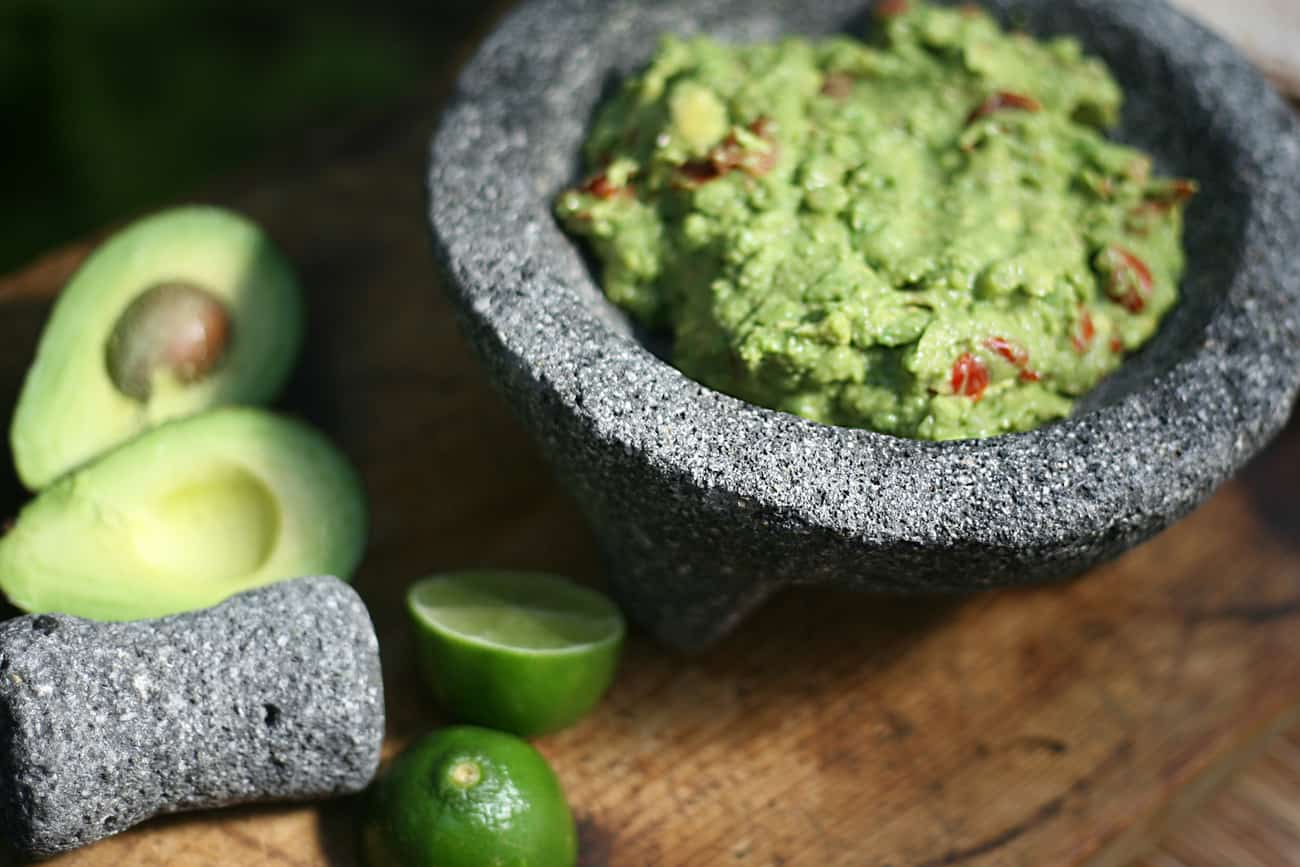 molcajete filled with homemade guacamole and a halved avocado and lime to the side.