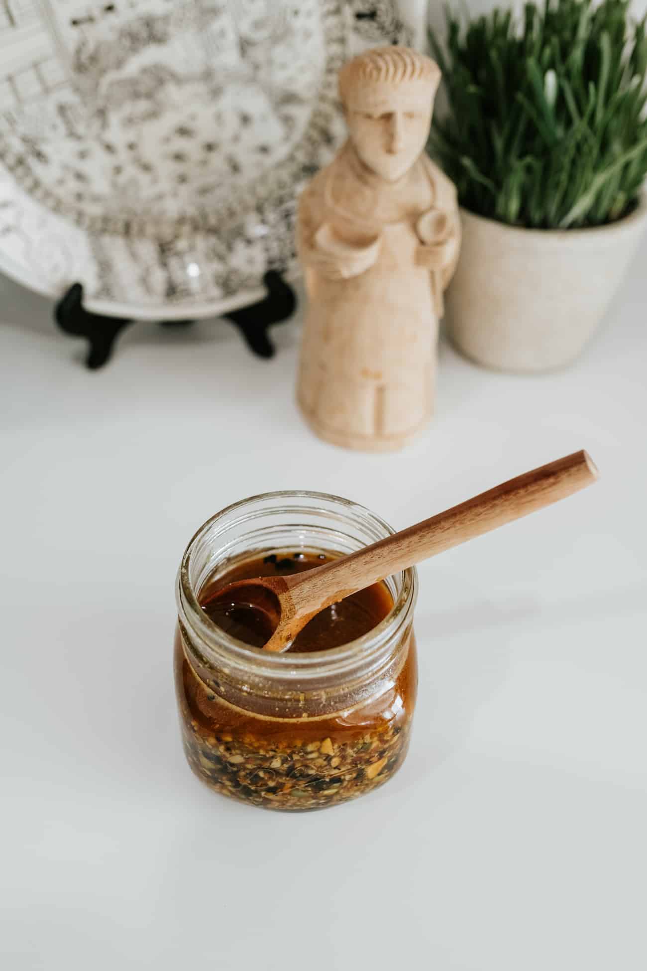 small mason jar of salsa macha with a wooden condiment spoon, with a small terracotta statue of a man in the background.