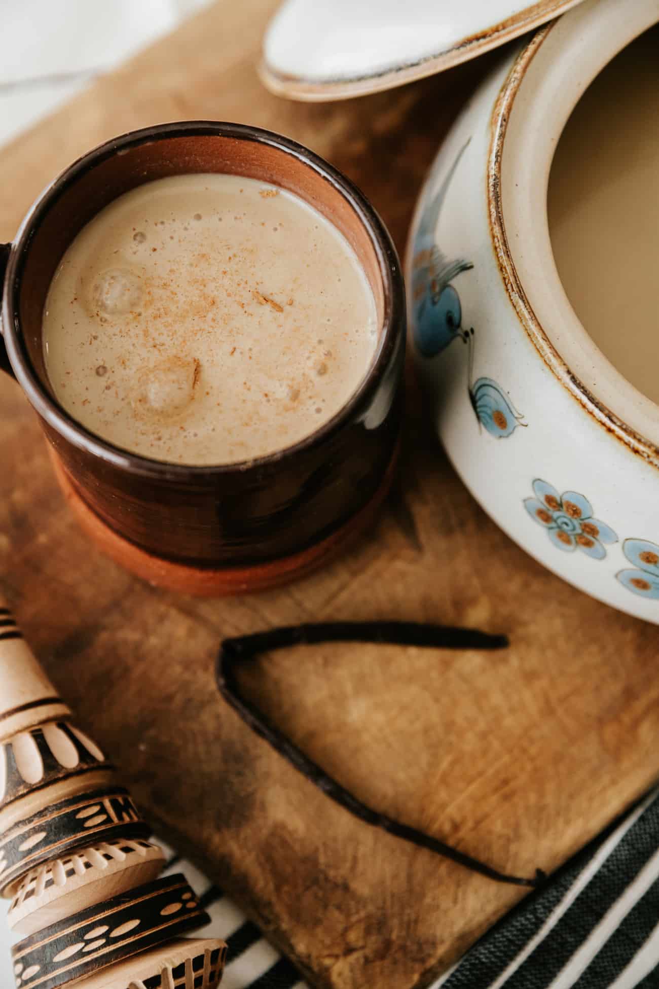 close up shot of mug of atole de vainilla in a brown mug on a wooden board with a vanilla bean.