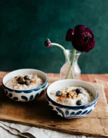 two blue and white bowls filled with avena and topped with blueberries and walnuts on a wooden tray for breakfast in bed.