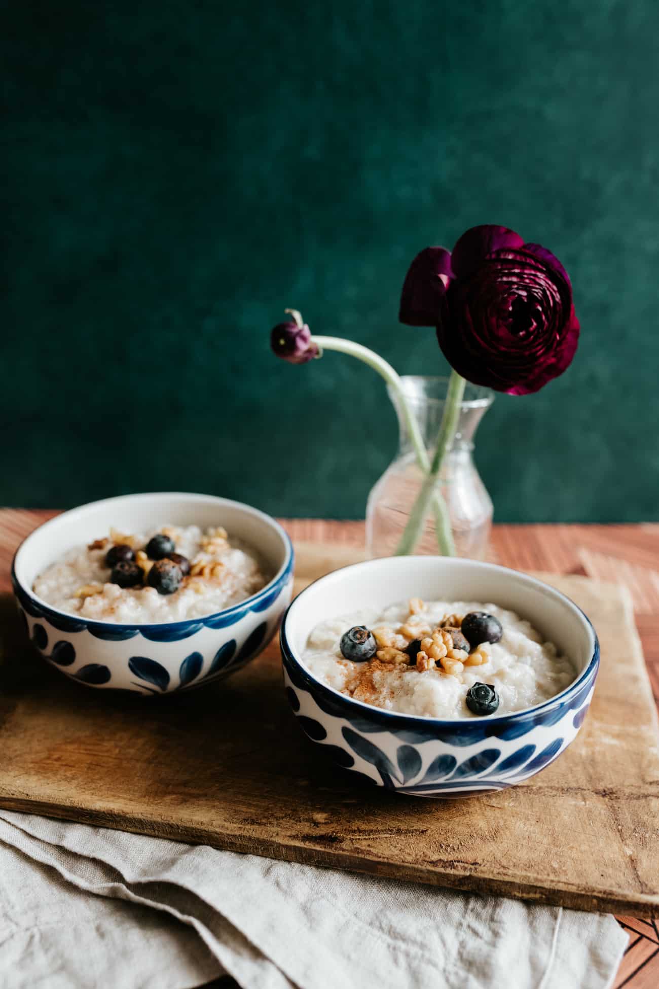 Old fashioned Mexican oatmeal (avena) in two blue and white painted bowls garnished with walnuts and blueberries. Renecula flower in a vase in the background.