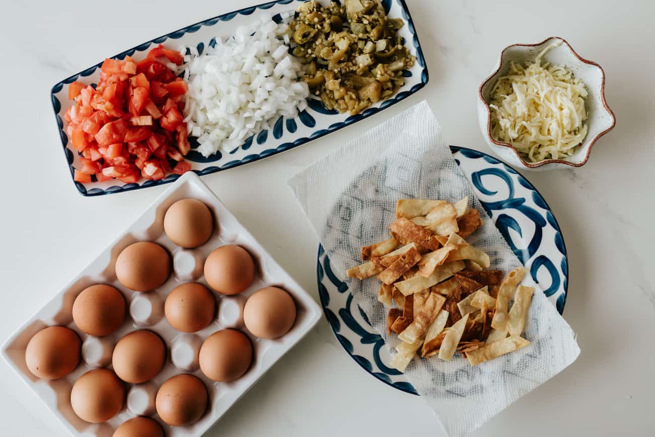 tomatoes, onions, roasted chiles, cheese, eggs and crispy tortilla strips laid out for making Tex Mex migas.