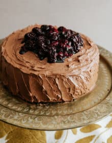 double layered chocolate cake with mocha buttercream and roasted berries on a gold cake stand.