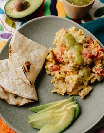 migas on a grey plate with avocado slices and toasted flour tortillas for making breakfast tacos.