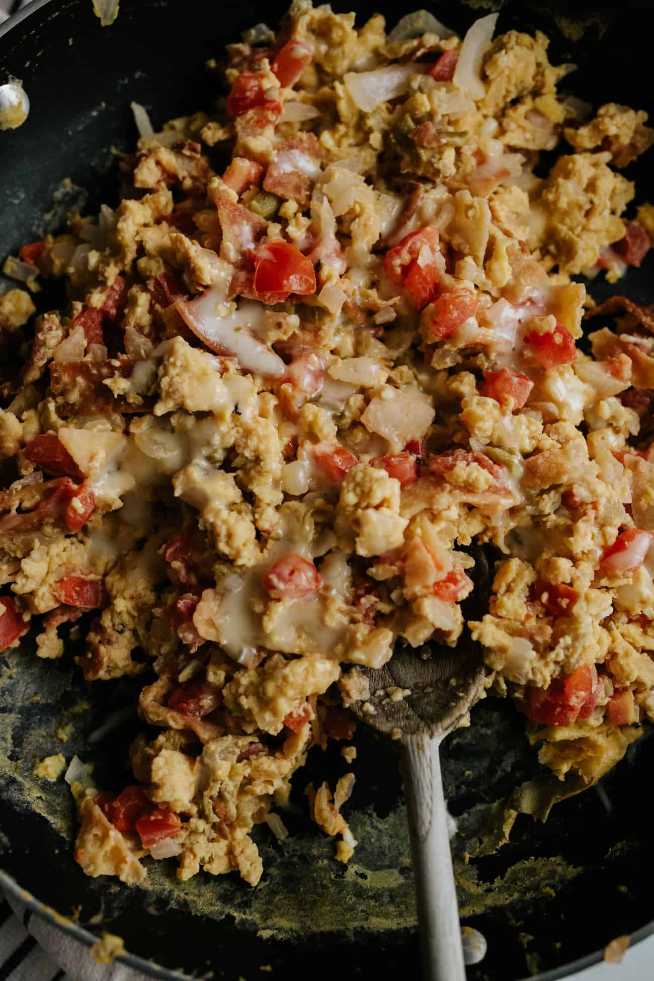 close up of cheesy breakfast migas in a pan with a wooden spoon.