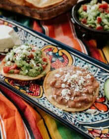 Vegetarian Mexican Tostadas With Refried Beans & Guacamole on a Mexican talavera platter on a striped fabric.