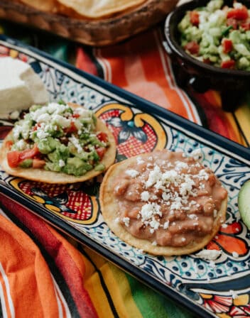 Vegetarian Mexican Tostadas With Refried Beans & Guacamole on a Mexican talavera platter on a striped fabric.