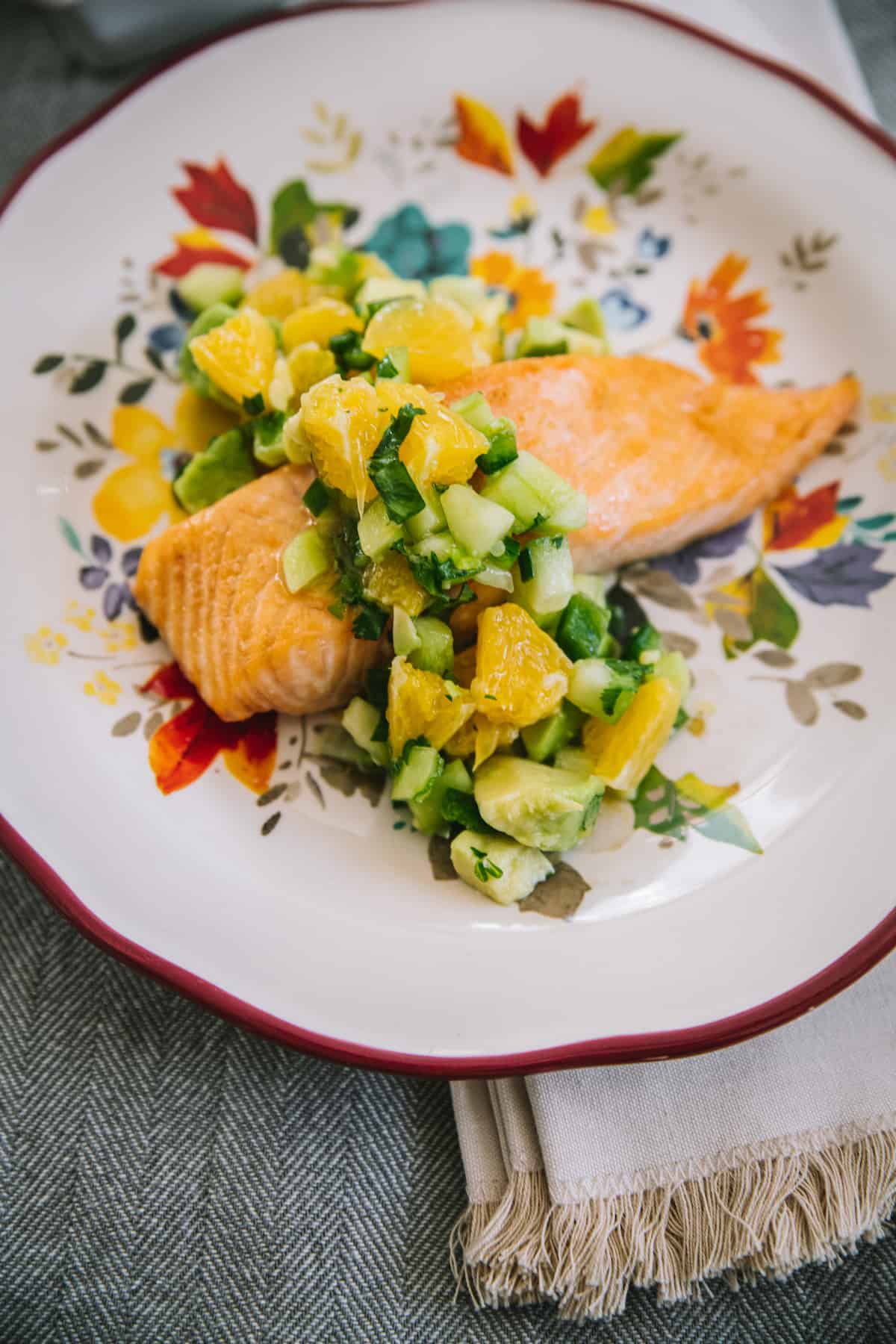 oven baked salmon topped with citrus avocado salsa on a white plate with red edges and a floral pattern.
