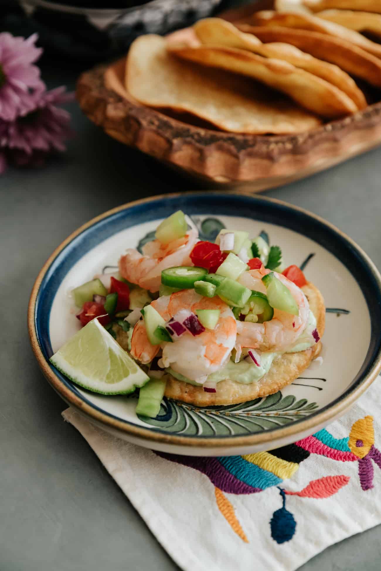 shrimp ceviche topped on a tostada on a painted Mexican plate and tostadas in the background.