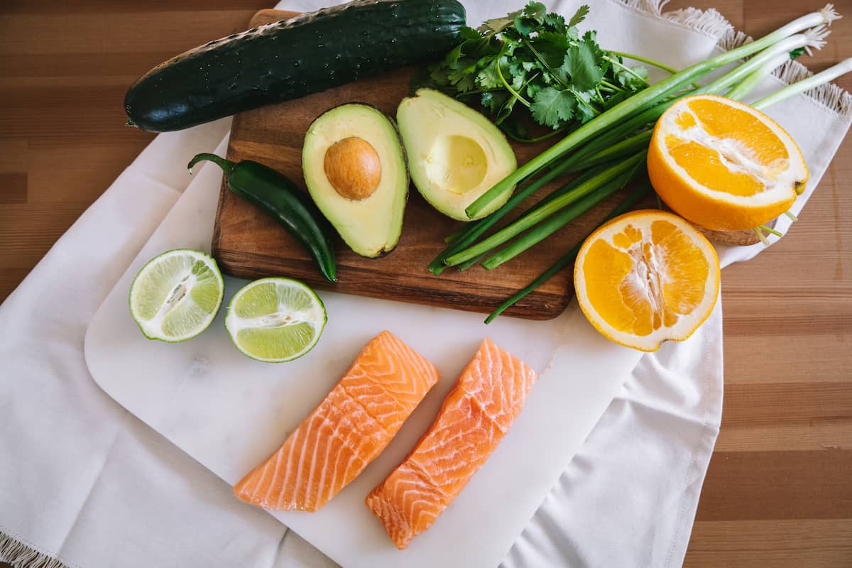 overhead shot of all ingredients needed to make oven baked salmon with citrus avocado salsa on a kitchen work surface.