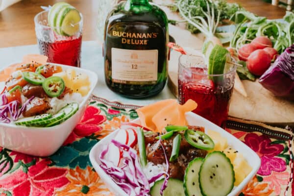 poke tuna bowls on a table with hibiscus whisky sours and a bottle of buchanan's whisky.