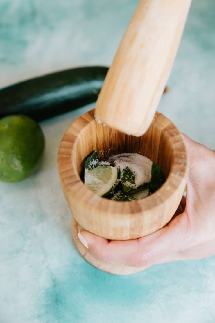 muddling mint, truvia, and limes in a wooden mortar and pestle. 