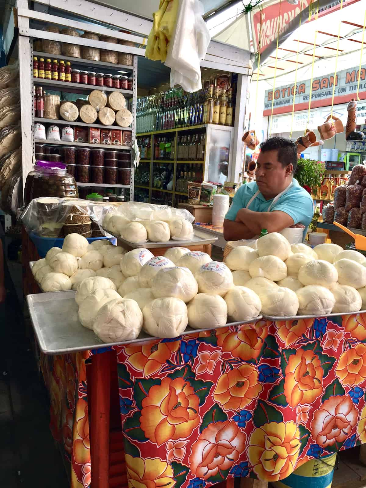 Mexican man selling balls of queso oaxaca in a market.