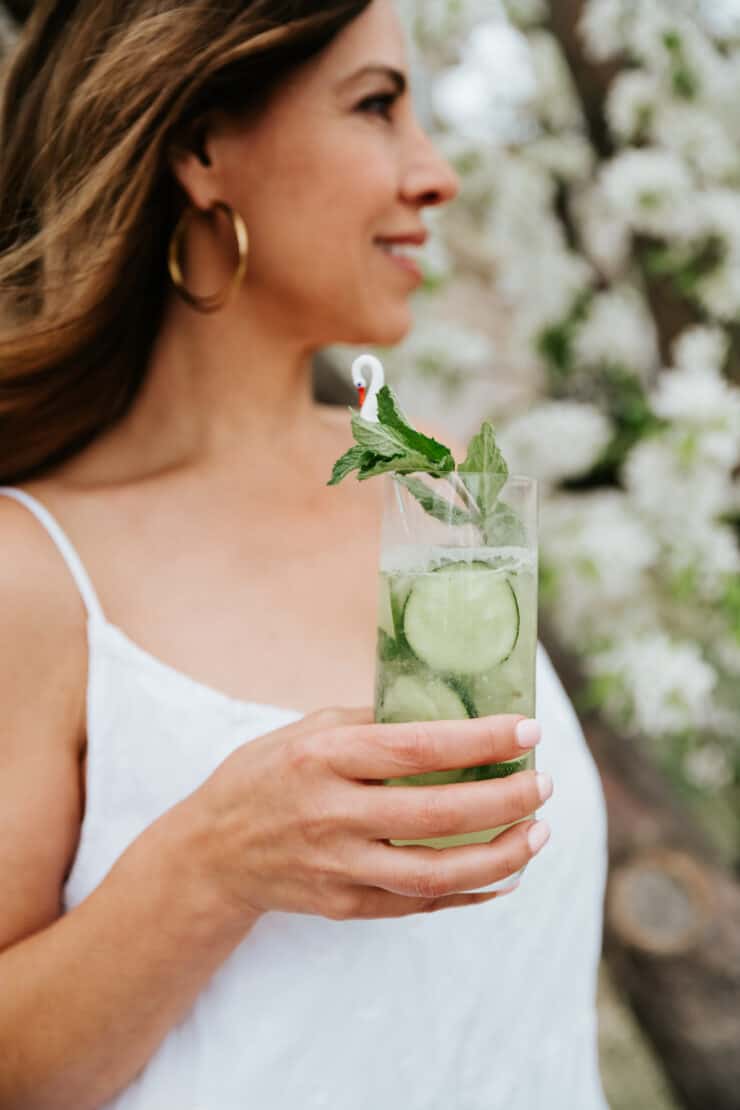Latina blogger holding a collins glass of cucumber mint mojito garnished with fresh mint. 
