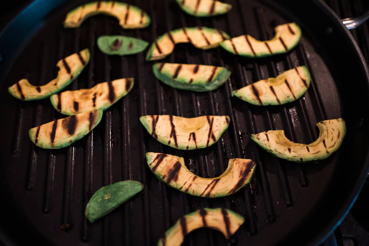 slices of avocado on a cast iron grill pan getting grilled.