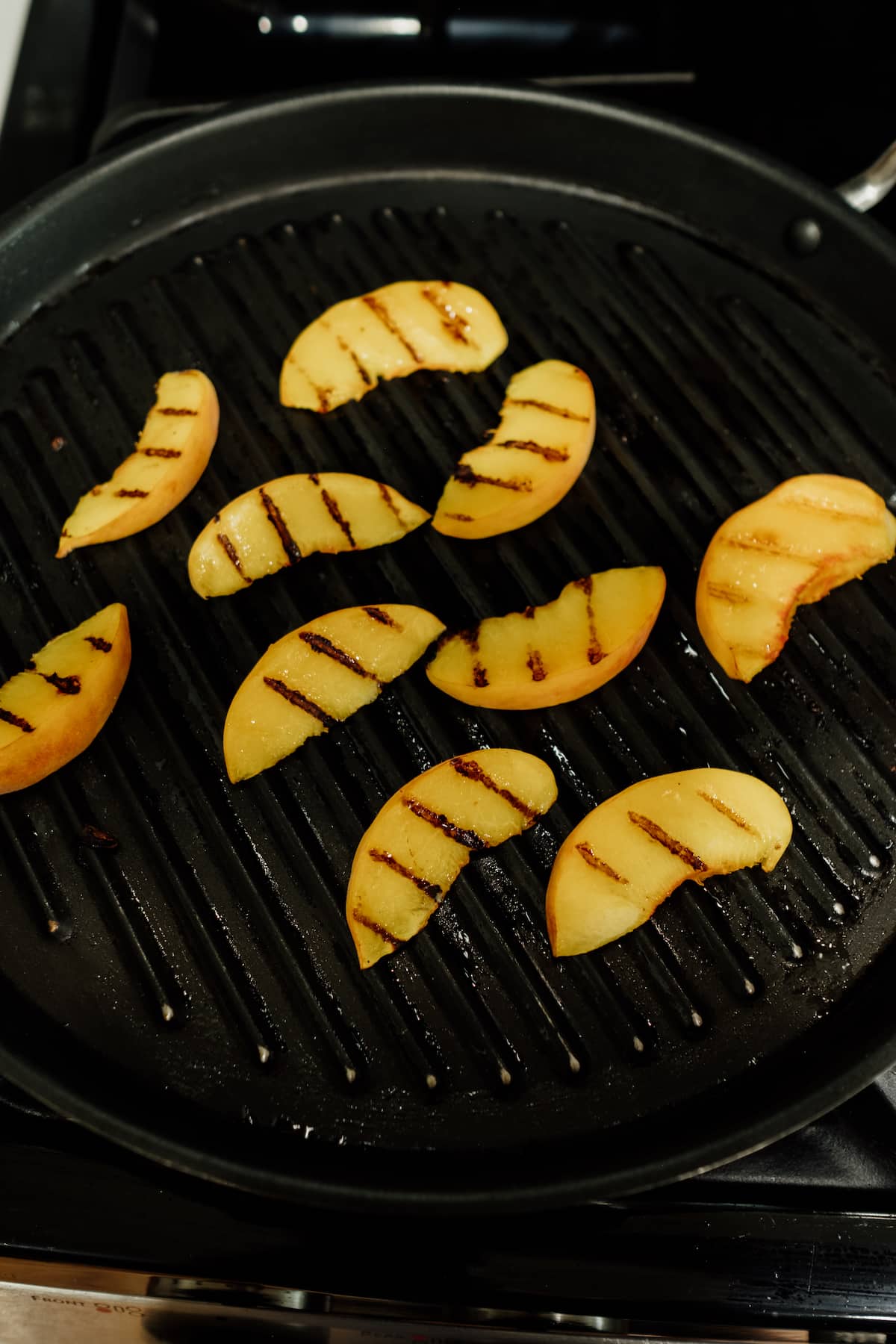 slices of peaches getting grilled on a grill pan.