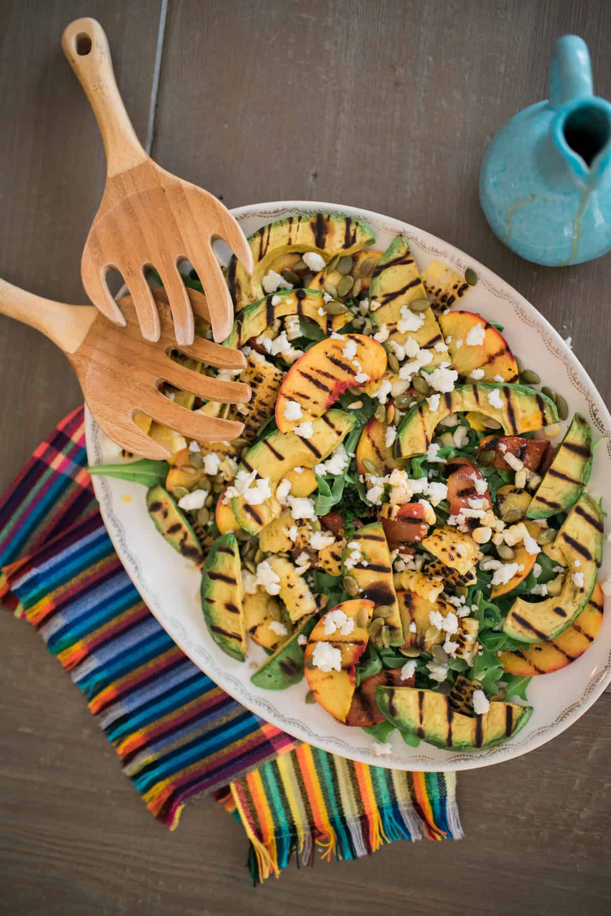 large serving platter of salad with grilled corn, avocado, and stone fruit garnished with queso panela. 