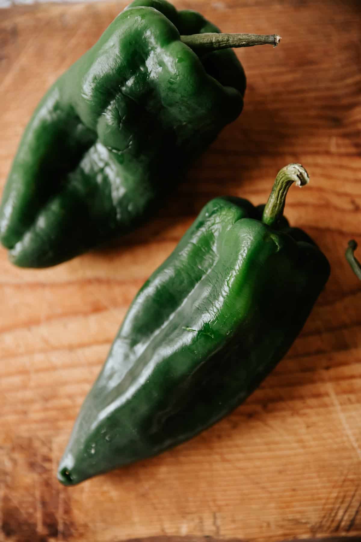 2 whole green poblano chiles on a wooden surface.