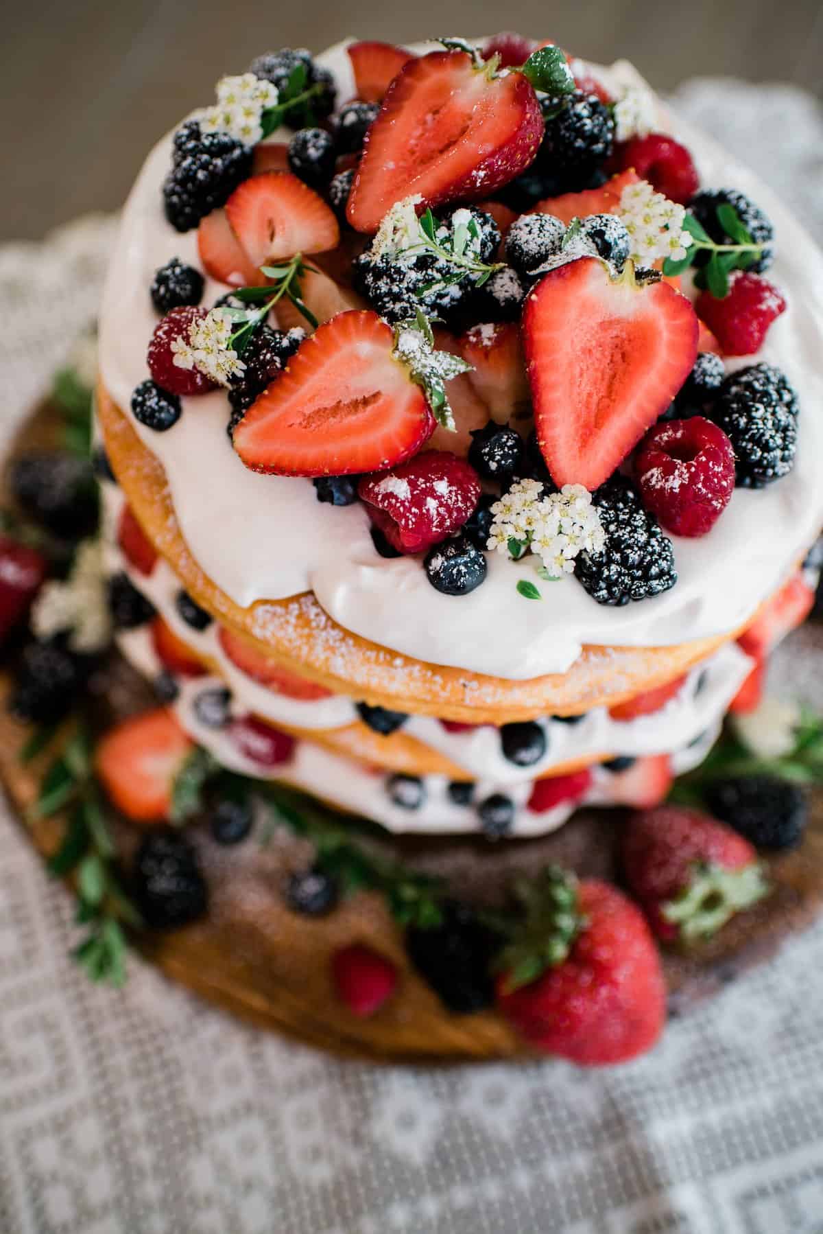overhead shot of the top of the lemon berry spring fling cake decorated with fresh berries, edible flowers and a light dusting of powdered sugar. 
