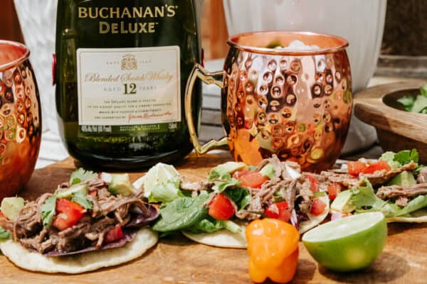 copper cup with whisky mule, bottle of Buchanan's whisky, and a platter of sapicon de res tostadas.