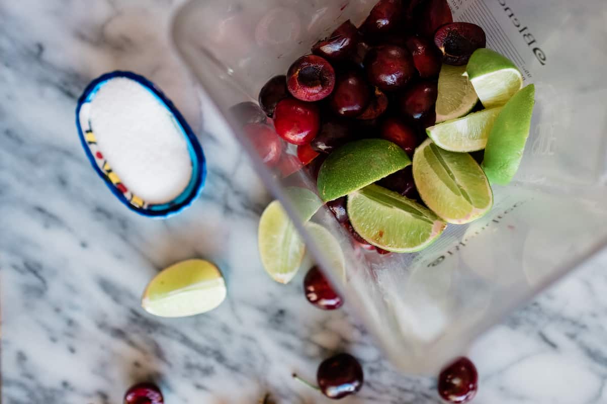 fresh pitted cherries and quartered limes in a blender pitcher. 