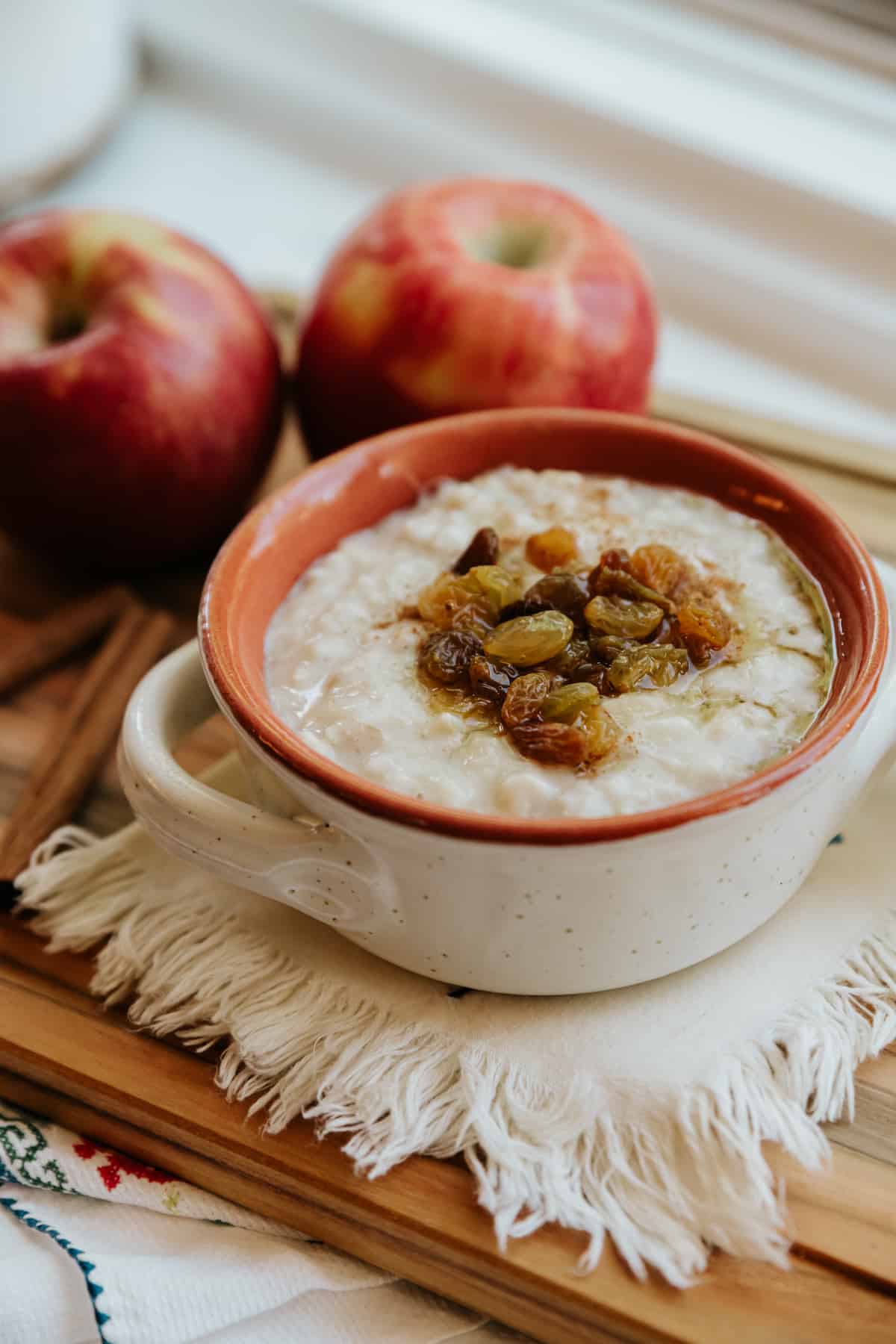 white and terracotta bowl with handles filled with mexican oatmeal and topped with a cinnamon apple raisin compote. 