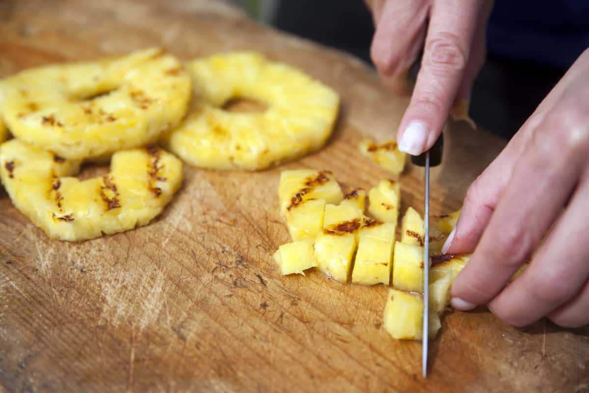 chopping grilled pineapple on a wooden cutting board.