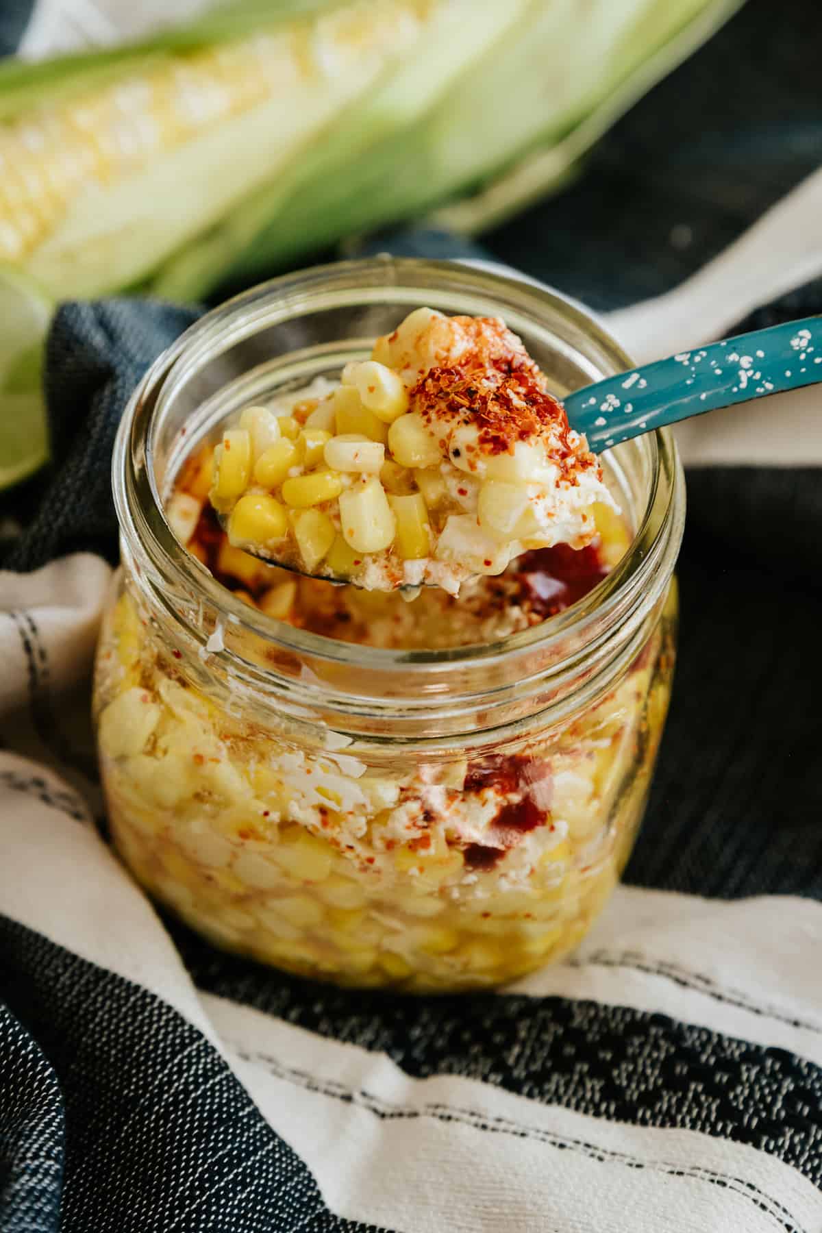 short mason jar filled with elote en vaso (a.k.a. esquites) and garnished with chili powder. 