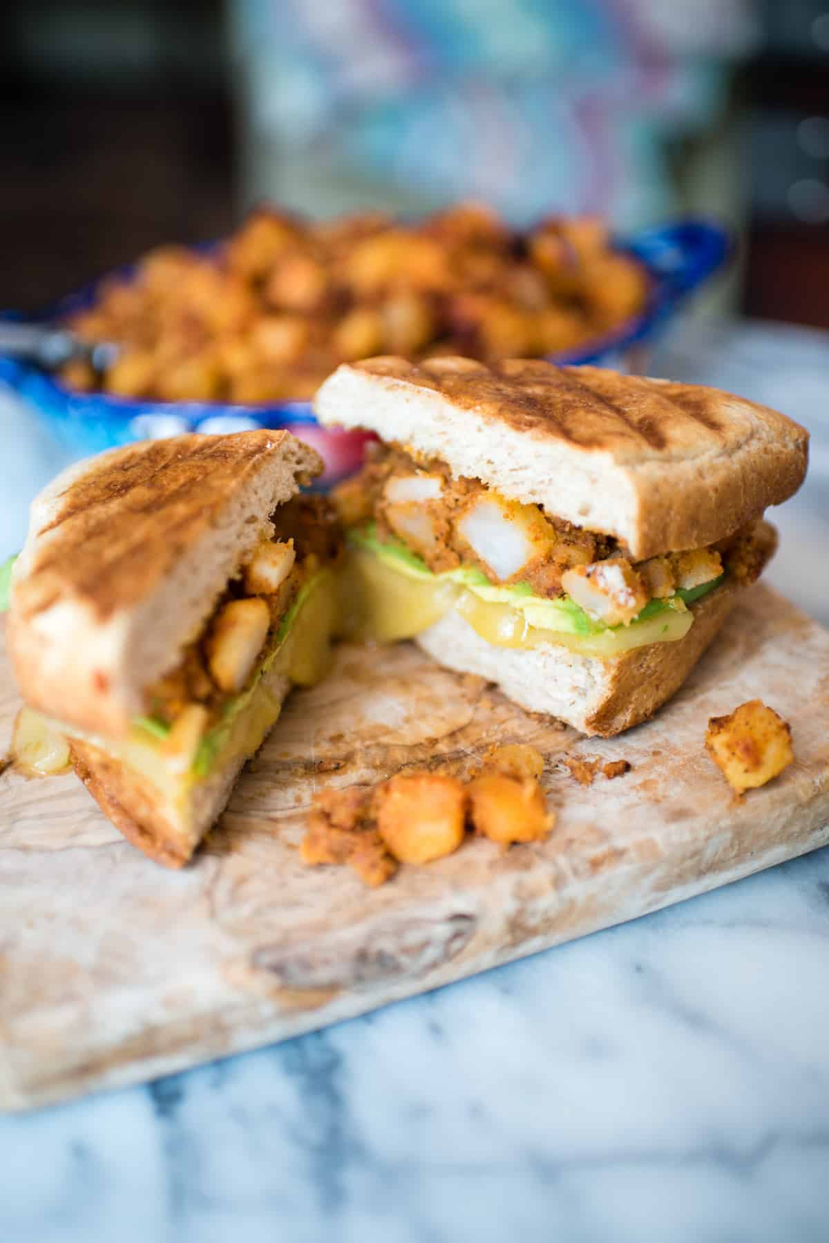 Breakfast Tortas with Potatoes and Chorizo cut in half with melted cheese on a cutting board.