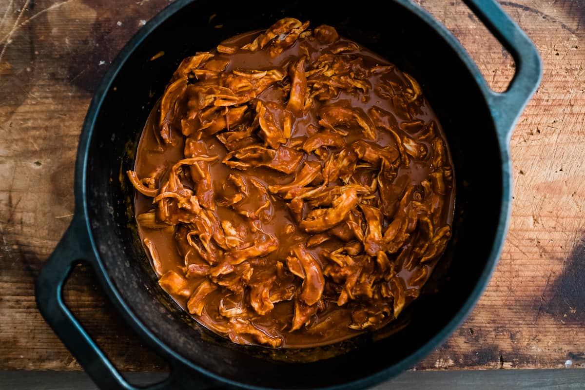 overhead shot of shredded chicken tamale filling mixed with mole sauce in a cast-iron skillet. 