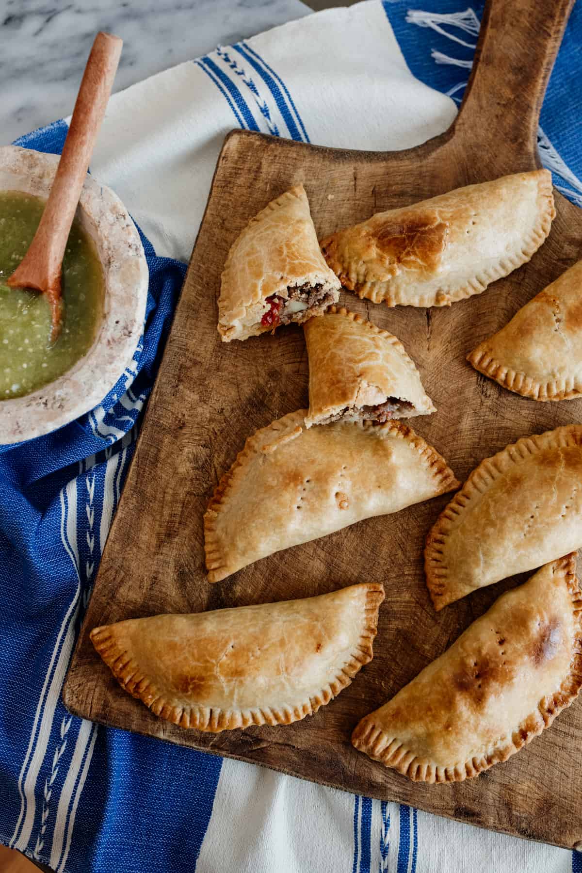 Mexican Picadillo Empanadas on a wooden board with a side of salsa verde on a blue Mexican linen