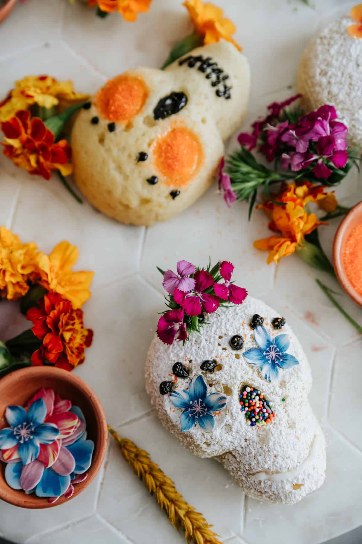 close up on a lemon skull cake dusted with powdered sugar and decorated with blue flowers for eyes and sprinkles for a nose with edible purple flowers as a crown.