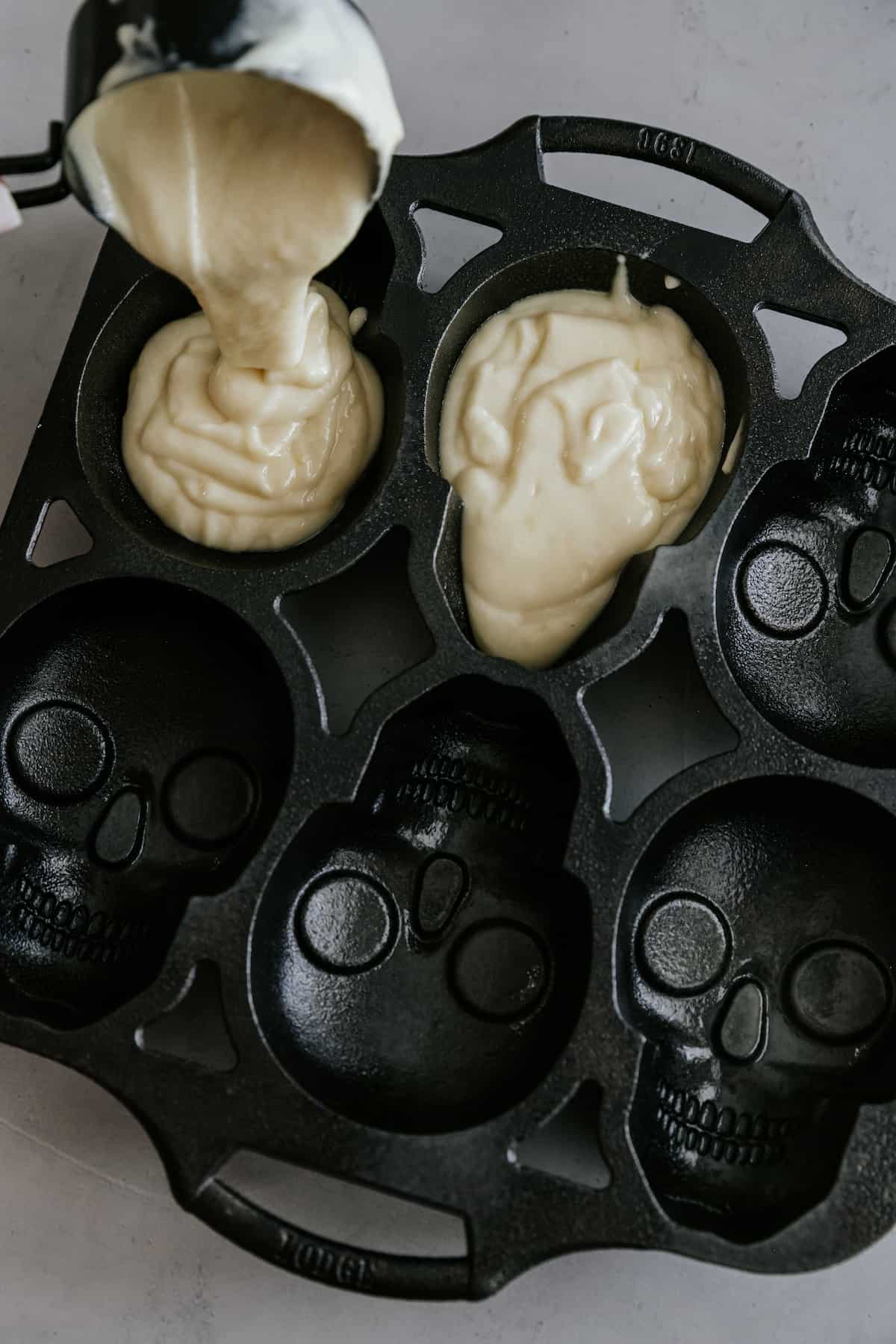 using a disher to pour batter into the skull cake pan mold.