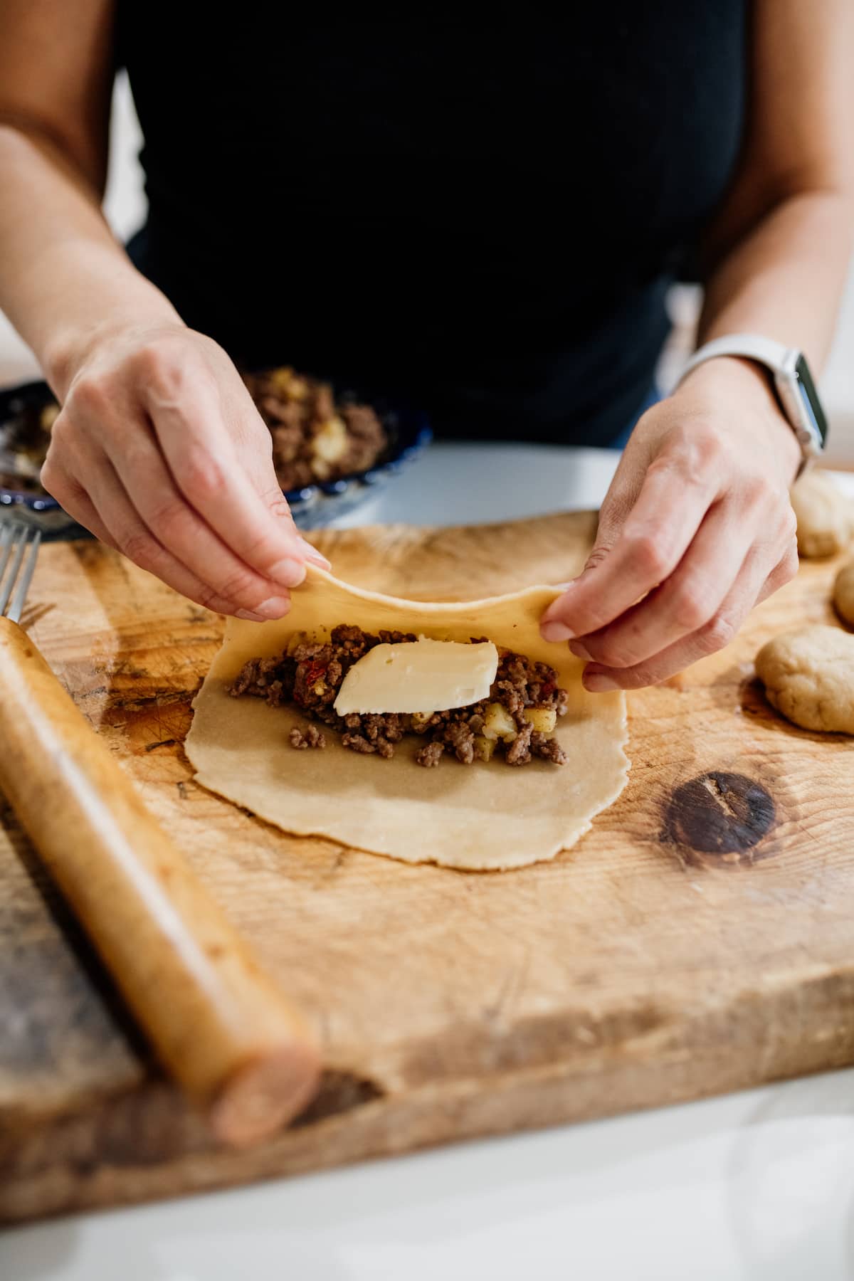 empanada disk being filled with picadillo and a slice of cheese and folded over with hands.