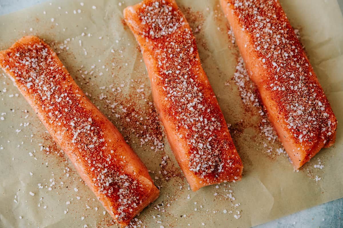 filetes de salmón en una bandeja forrada con pergamino y espolvoreados con condimentos para tacos. 