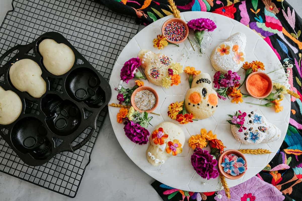 zoomed out view of sugar skull cake decorating table with different bowls of sprinkles and edible flowers.