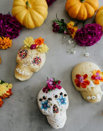 overhead shot of lemon mini skull cakes on a white table, with each decorated slightly differently with powdered sugar, edible writing gel, and sprinkles.
