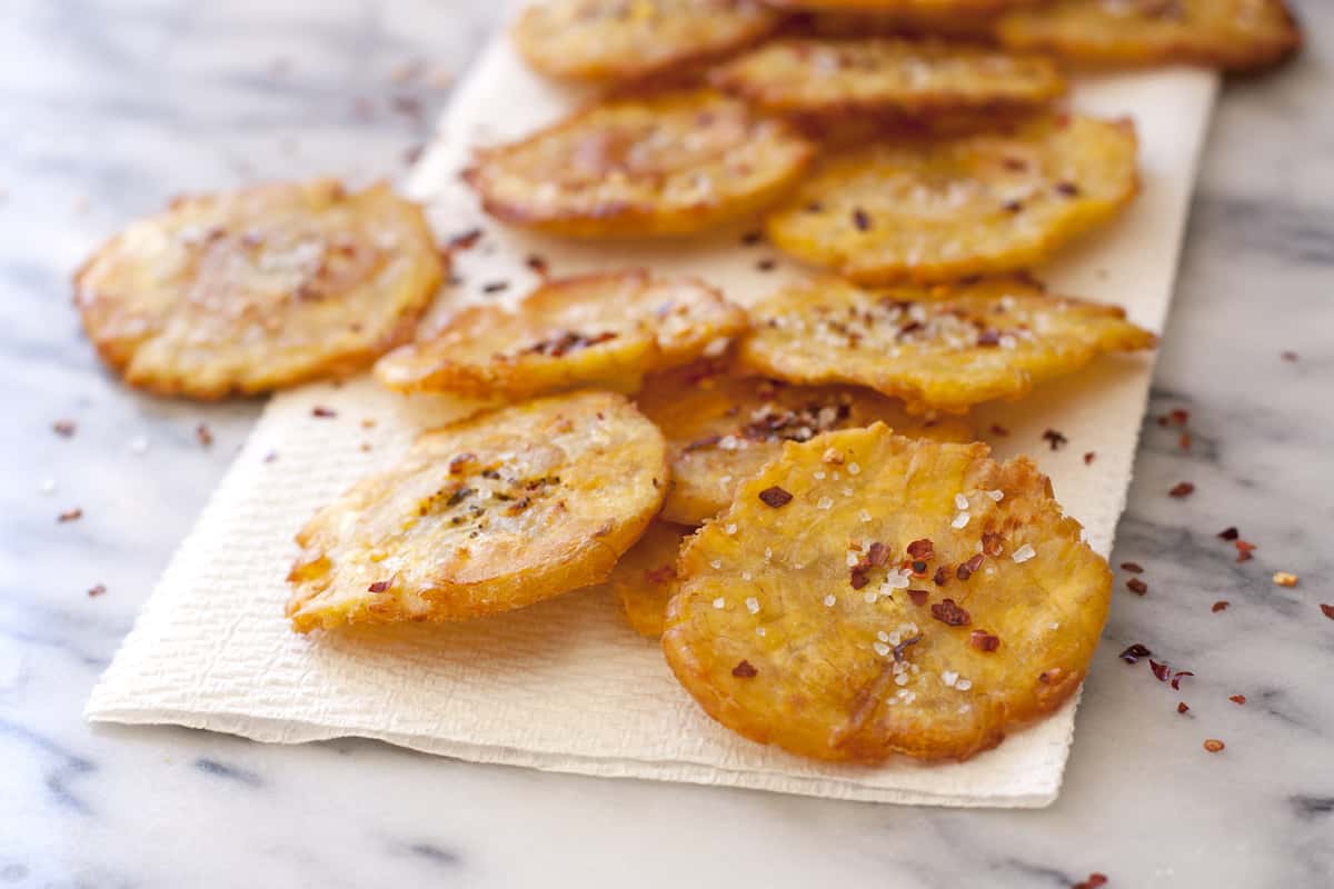 tostones after second fry are drying on a paper towel and have been sprinkled with salt and red pepper flakes.