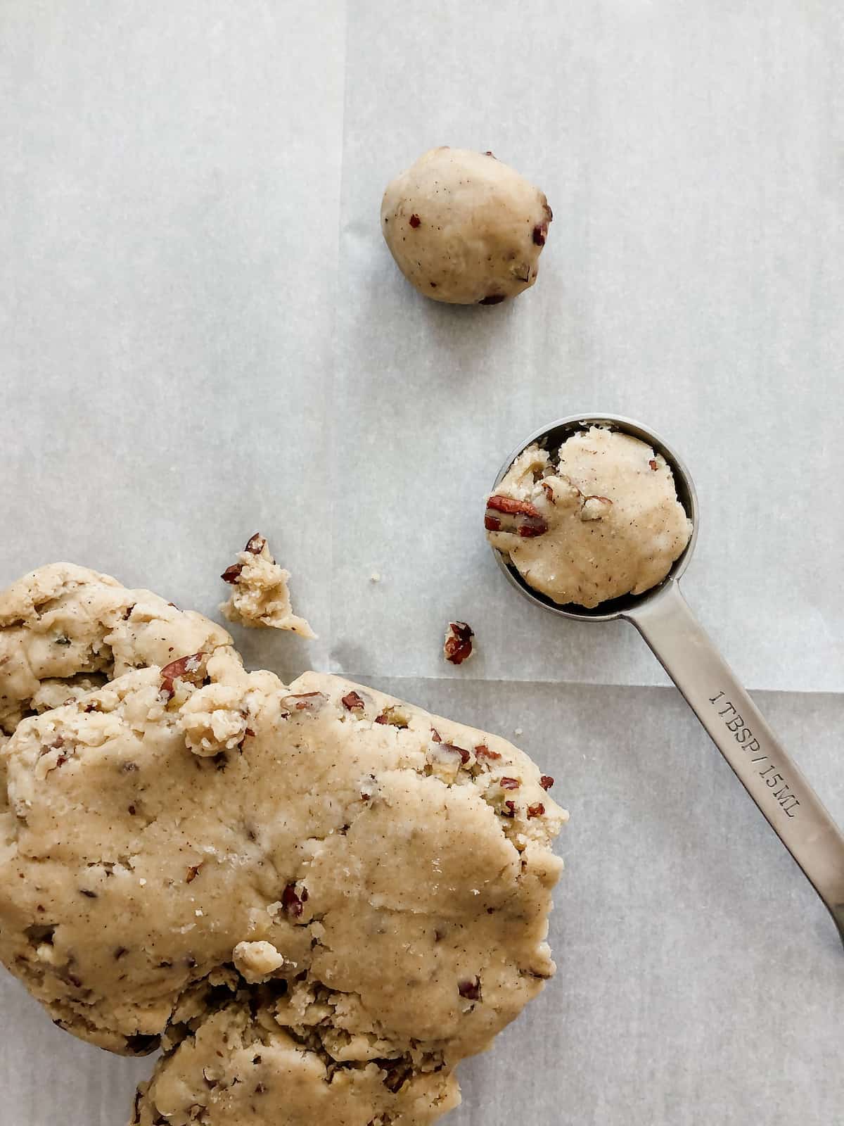 butter pecan thumbprint cookie dough being scooped onto parchment-lined cookie sheet for baking. 