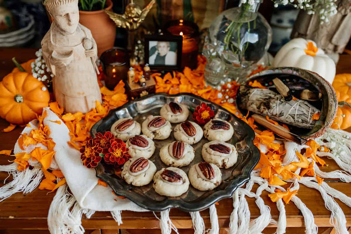 Dia de Muerto altar with a silver platter of double pecan thumbprint cookies, marigolds, an abalone shell with a sage smudge stick, and a photo of the author's grandma.