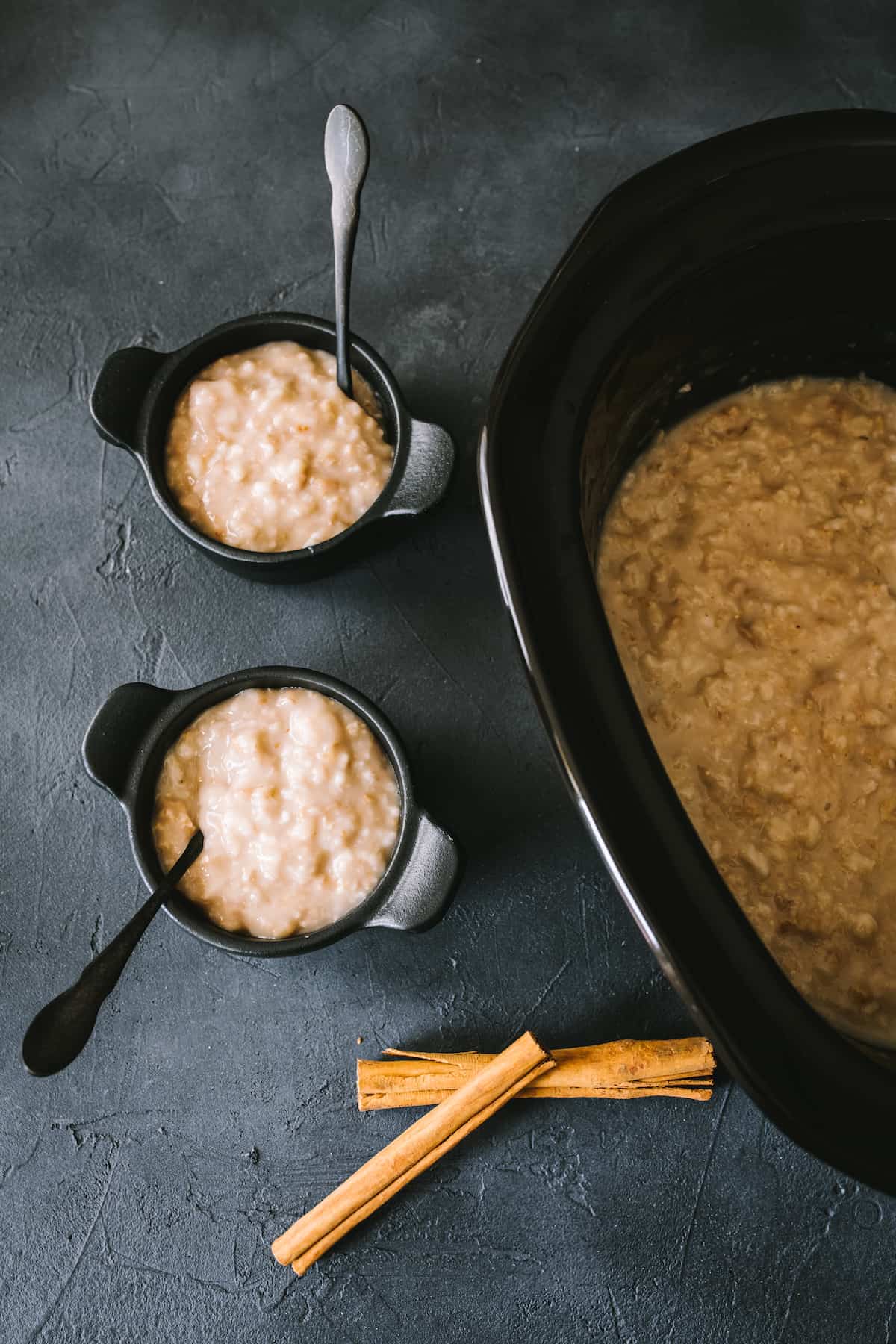 oatmeal made in a slow cooker with two black cast iron bowls served with oatmeal.