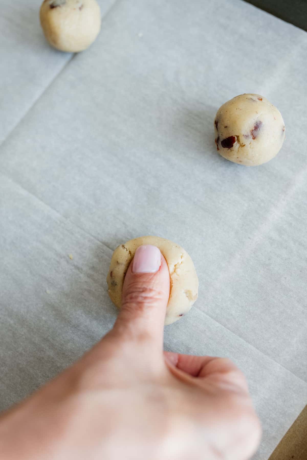 woman's thumb pressing down on a pecan cookie dough ball.