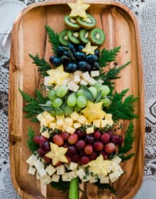 Christmas tree shaped cheese platter on a wooden tray kiwi grapes star fruit and cheese surrounded by evergreen branches.