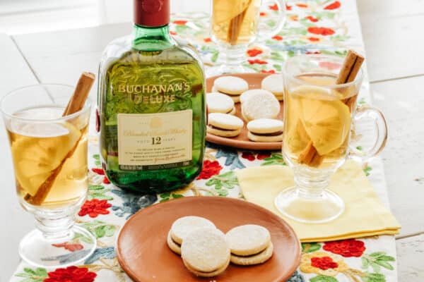 plate of alfajores cookies with a hot tea and whisky cocktail in the background with a bottle of buchanan's whisky.