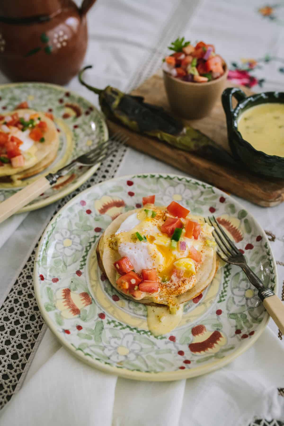 green and yellow plate with Mexican Eggs Benedict with Chile Verde Hollandaise on a breakfast table. 