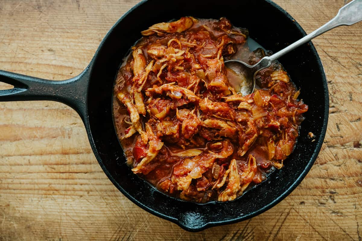 overhead shot of shredded chicken tinga in a cast iron skillet.